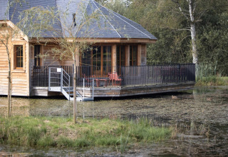 Wooden lodge named 'Happiness' in Belgium, featuring a deck over the water and surrounded by nature.