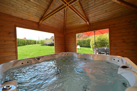 Indoor hot tub in a wooden lodge with large windows showing garden and terrace at Ard Zen in Belgium.