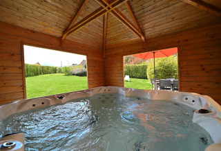 Indoor hot tub in a wooden lodge with large windows showing garden and terrace at Ard Zen in Belgium.