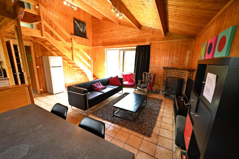 Wood-paneled living room at Ard Zen lodge in Belgium, with modern furniture, fireplace and staircase.