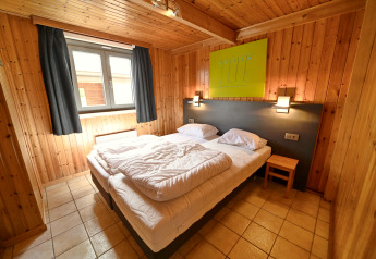 Knusse slaapkamer in Ard Zen lodge in België met houten wanden, tweepersoonsbed en raam.