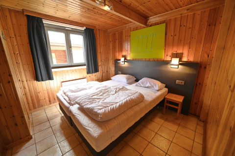 Cozy bedroom at Ard Zen lodge in Belgium with wooden walls, double bed, tile floor, and window.