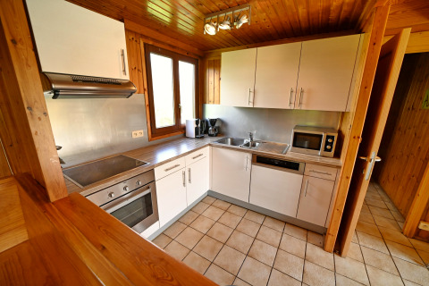 Cuisine moderne de lodge avec placards blancs, four, micro-ondes et décor en bois à Ard Zen en Belgique.