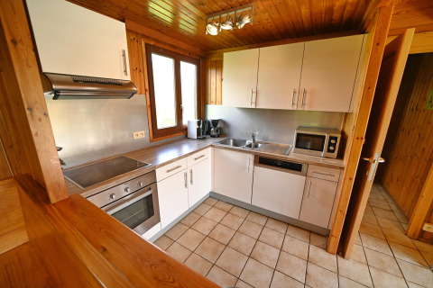 Modern lodge kitchen with white cabinets, oven, microwave, and wooden decor at Ard Zen in Belgium.