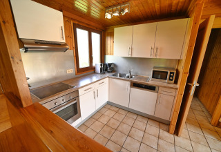 Modern lodge kitchen with white cabinets, oven, microwave, and wooden decor at Ard Zen in Belgium.