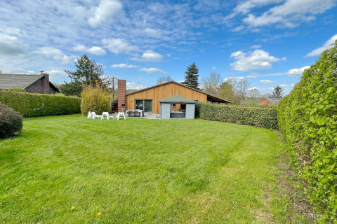 Spacious lawn with hedge, patio seating, and blue sky in front of Ard Zen lodge surrounded by greenery.