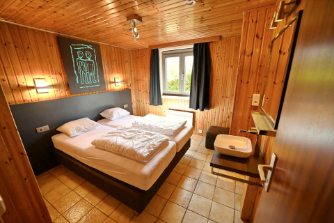 Chambre chaleureuse au lodge Ard Zen en Belgique avec lit double, murs en bois et fenêtre.