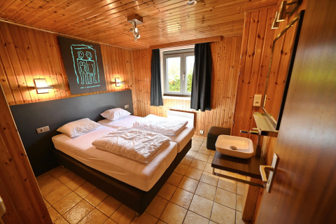 Cozy room at Ard Zen lodge in Belgium featuring a double bed, wood-paneled walls, and a window.