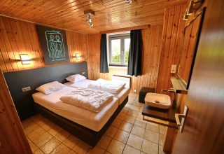 Cozy room at Ard Zen lodge in Belgium featuring a double bed, wood-paneled walls, and a window.