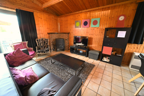 Salon avec murs en bois, canapé en cuir noir, cheminée, TV et déco colorée au lodge Ard Zen en Belgique.