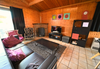 Salon avec murs en bois, canapé en cuir noir, cheminée, TV et déco colorée au lodge Ard Zen en Belgique.