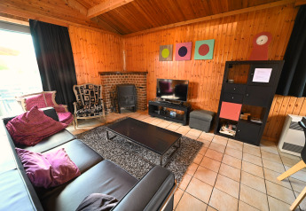 Woonkamer met houten wanden, zwarte leren bank, open haard, tv en decoratie in Ard Zen lodge, België.