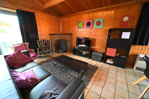 Living room with wood panel walls, black leather sofa, fireplace, TV and decor at Ard Zen lodge in Belgium.