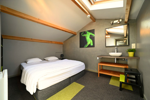 Chambre moderne sous les toits du lodge Ard Zen en Belgique avec lit double et puits de lumière.