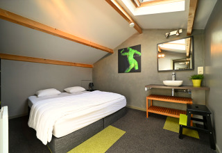 Chambre moderne sous les toits du lodge Ard Zen en Belgique avec lit double et puits de lumière.