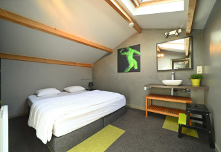 Modern attic bedroom at Ard Zen lodge in Belgium, featuring a double bed, skylights, and a wash area.