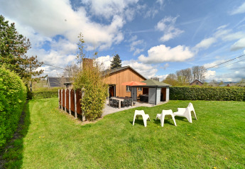 Buitenaanzicht van lodge Ard Zen in België met groen gras, terras, witte stoelen en blauwe lucht.