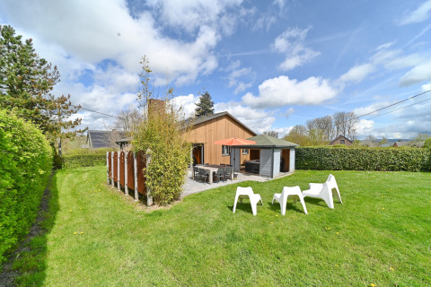 Outdoor view of Ard Zen lodge in Belgium with green lawn, terrace, tables, chairs, and a blue sky.