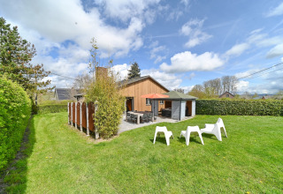 Outdoor view of Ard Zen lodge in Belgium with green lawn, terrace, tables, chairs, and a blue sky.