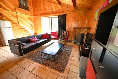 Salon du lodge «Ard Zen» en Belgique avec canapé noir, murs en bois, cheminée et mobilier moderne.