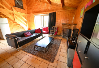 Salon du lodge «Ard Zen» en Belgique avec canapé noir, murs en bois, cheminée et mobilier moderne.