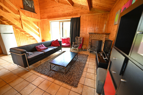 Living room at lodge «Ard Zen» in Belgium, featuring black sofa, wood interior, fireplace and TV.