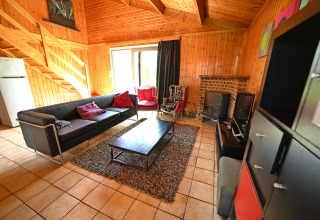 Living room at lodge «Ard Zen» in Belgium, featuring black sofa, wood interior, fireplace and TV.