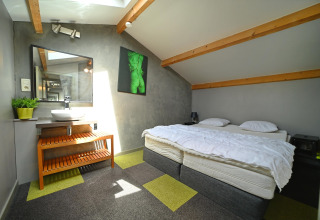 Bright room at Ard Zen lodge in Belgium, featuring a double bed, wood beams, and modern decor.