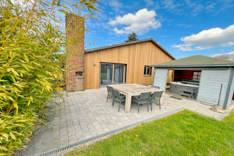 Espace extérieur de la lodge Ard Zen en Belgique, avec façade bois, table à manger, barbecue et spa couvert.
