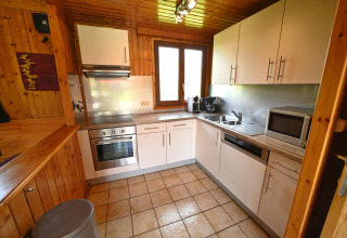 Modern kitchen with white cabinets, oven, microwave, and wood paneling at Ard Zen lodge in Belgium.