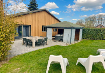 Foto van Ard Zen lodge in België met houten gevel, terrasmeubilair, tuinhuisje en groene tuin.