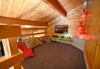 Mezzanine chaleureuse en bois, coussins, TV et éclairage dans le lodge Ard Zen en Belgique.