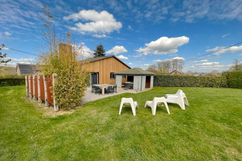Vue extérieure du lodge Ard Zen en Belgique avec pelouse verte, terrasse et chaises de jardin blanches.