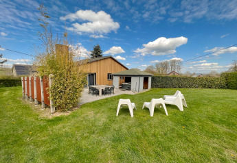 Buitenaanzicht van Ard Zen lodge in België met gazon, terras en ligstoelen onder een blauwe lucht.