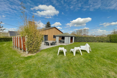 Outdoor view of the Ard Zen lodge in Belgium featuring a green lawn, patio, and relaxing chairs.