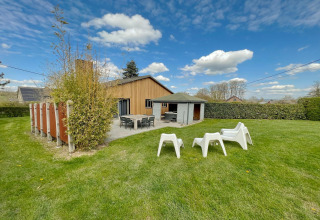 Outdoor view of the Ard Zen lodge in Belgium featuring a green lawn, patio, and relaxing chairs.