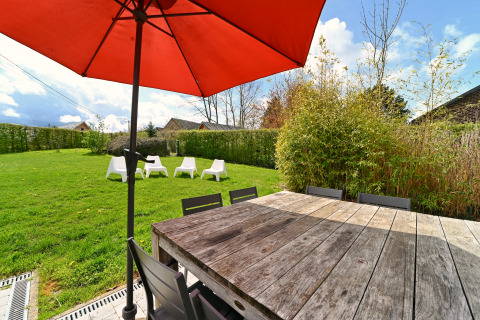 Espace extérieur de la lodge Ard Zen en Belgique, avec table en bois, parasol rouge et jardin verdoyant.