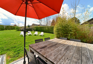 Espace extérieur de la lodge Ard Zen en Belgique, avec table en bois, parasol rouge et jardin verdoyant.