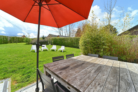 Outdoor dining at Ard Zen lodge in Belgium, showing a wooden table, red umbrella, and garden chairs.