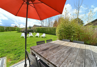 Outdoor dining at Ard Zen lodge in Belgium, showing a wooden table, red umbrella, and garden chairs.