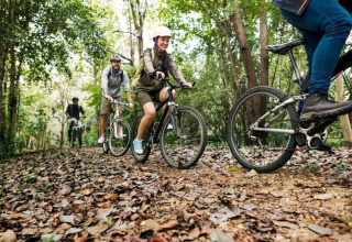 Groupe de personnes faisant du vélo sur un sentier forestier couvert de feuilles au lodge Ard Zen en Belgique.