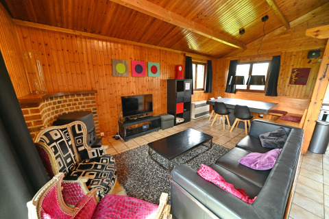 Living room at Ard Zen lodge in Belgium with wood walls, black sofa, eclectic chairs and dining area.