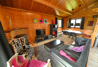 Living room at Ard Zen lodge in Belgium with wood walls, black sofa, eclectic chairs and dining area.