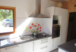 Moderne keuken met witte kasten, kookplaat, oven, magnetron en een raam met zicht op auto en natuur.