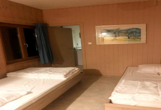 Eenvoudige lodgekamer in Les Peupliers de la pecherie in België, met twee bedden en open deur.