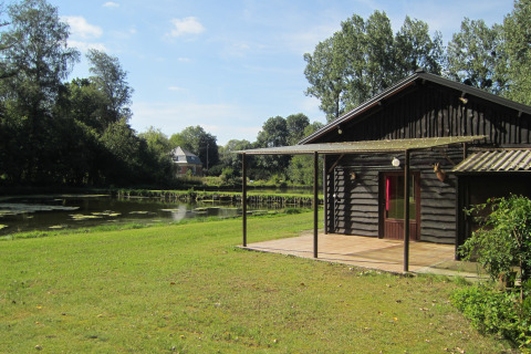 Houten lodge aan vijver bij Les Peupliers de la pecherie, België, omgeven door bomen en groen.