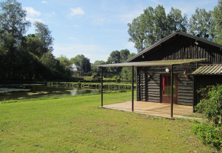 Houten lodge aan vijver bij Les Peupliers de la pecherie, België, omgeven door bomen en groen.