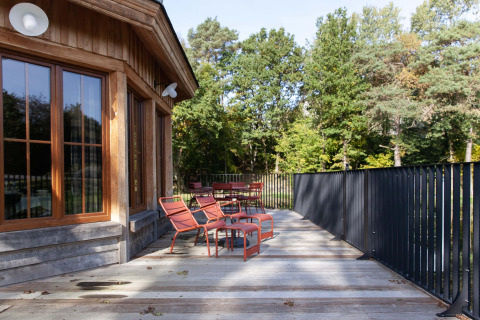 Outdoor deck at Cabane The Funny Friends lodge, featuring red chairs and a view of lush, green forest.