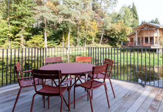 Outdoor terrace with table and chairs at Cabane The Funny Friends in Belgium, overlooking the woods and lodge.