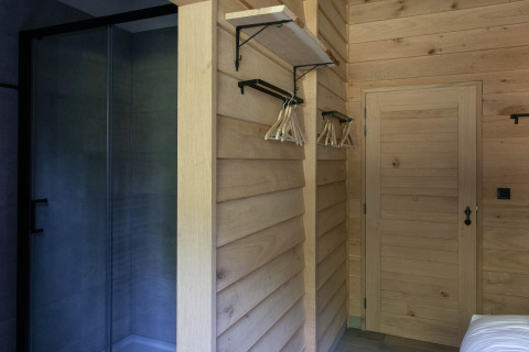 Interior revestido de madera con estante, perchas y ducha de cristal en una cabaña en Bélgica.